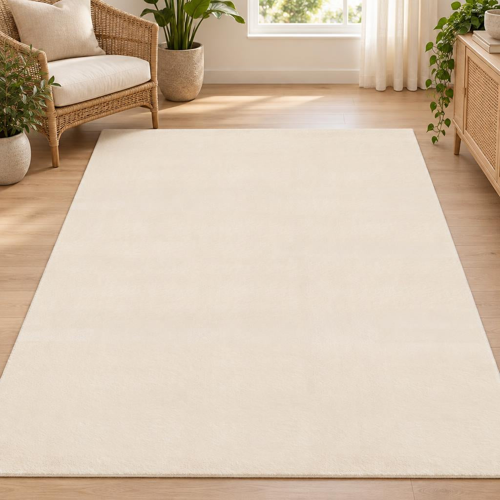 Effen vloerkleed Cozy Beige, laagpolig in licht zandbeige, bij een rotan fauteuil – sfeerimpressie in de woonkamer