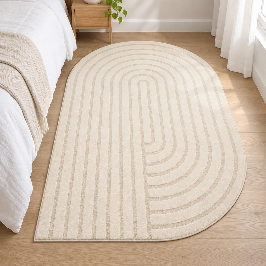 Vloerkleed Elio 2306 Crème met boogreliëf in organische vorm naast een wit bed – sfeerimpressie in de slaapkamer