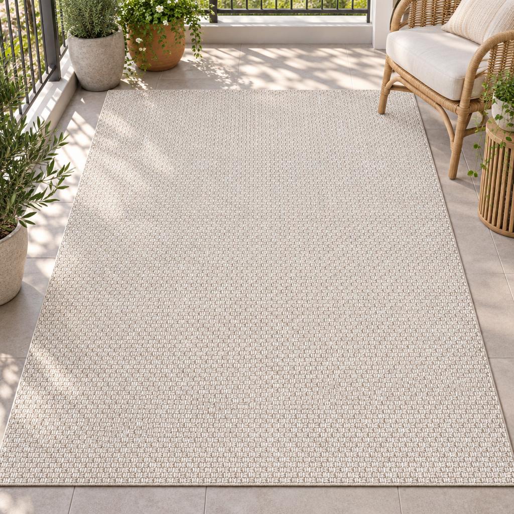 Vloerkleed Helsinki Beige met fijne mandweving, naast een rotan loungestoel tussen de planten – sfeerimpressie op het balkon