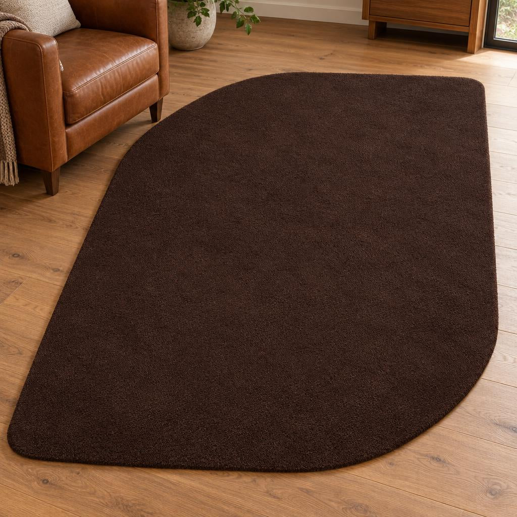 Vloerkleed Loft Shape 46 Bruin in organische bladvorm naast een cognac leren fauteuil – sfeerimpressie in de woonkamer