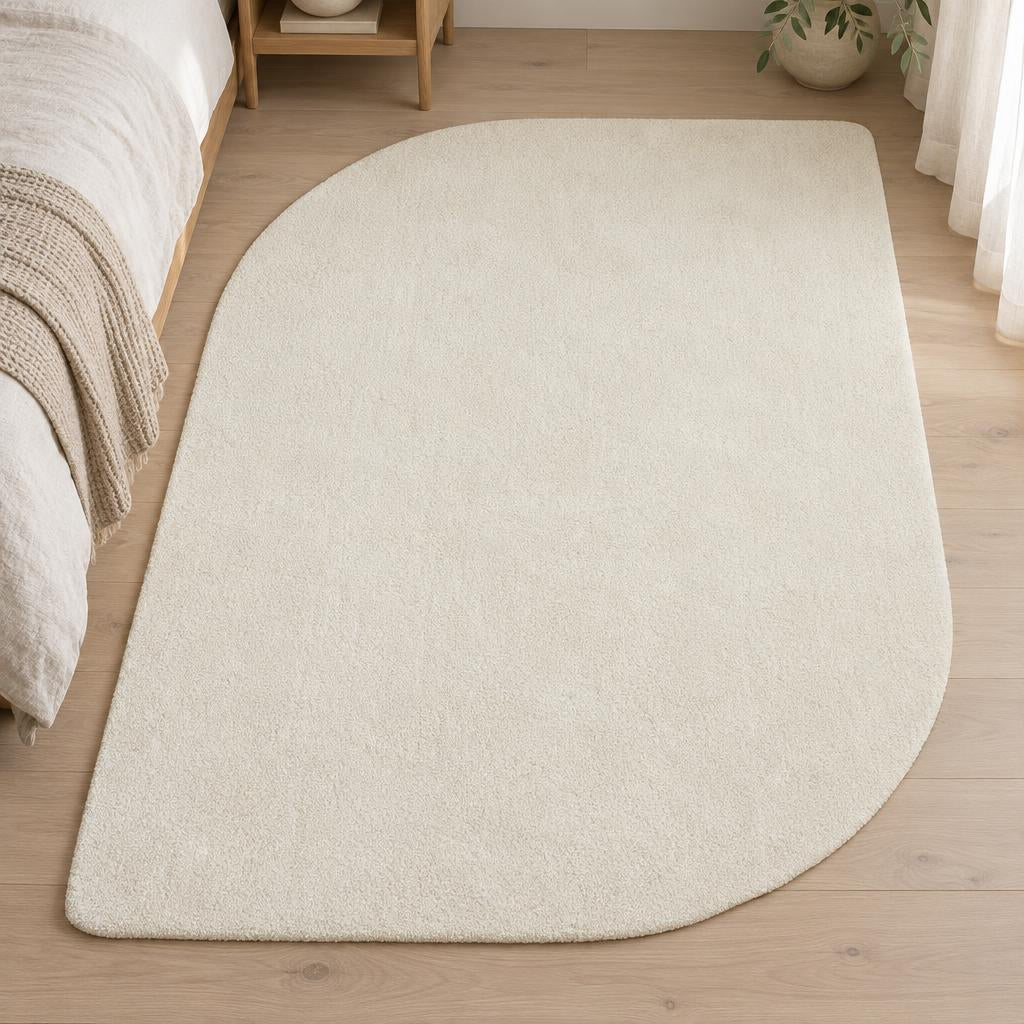 Effen vloerkleed Loft Shape 46 Crème in organische vorm naast een eiken bed – sfeerimpressie in de slaapkamer