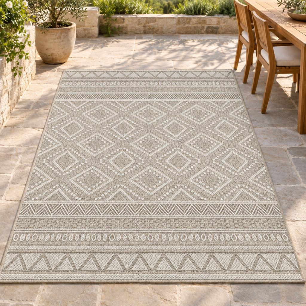 Vloerkleed Ottawa 22567 Beige met wit ruitenpatroon en zigzagranden naast een teakhouten tuinset – sfeerimpressie op het terras