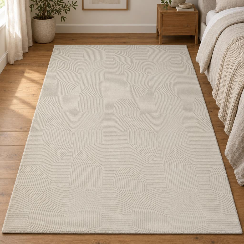 Vloerkleed Stilo 390 Crème met boog- en lijnenreliëf naast het bed – sfeerimpressie in de slaapkamer